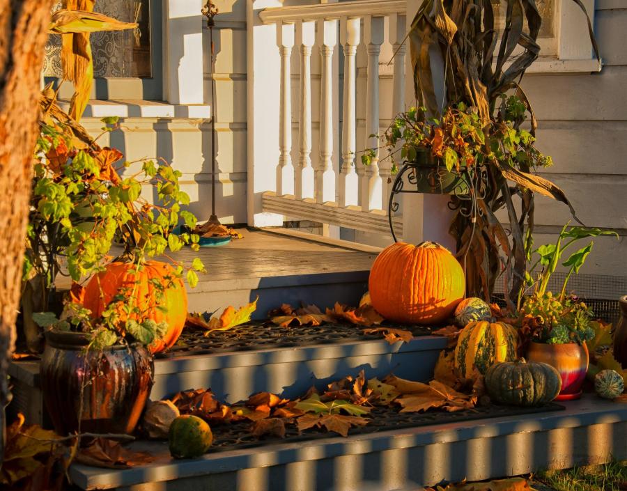 Welcoming front porch decorated with autumn pumpkins, a seasonal wreath, and warm lantern lighting.